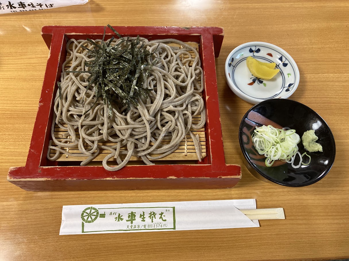 水車生そばのざるそば。赤い器に太めの田舎そばが盛られ、薬味とわさびが添えられている
