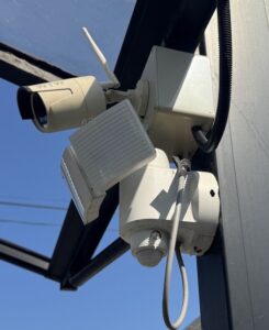 レンガの壁の角に取り付けた首振り式の屋外防犯カメラと、配線を通す管・電源ボックス