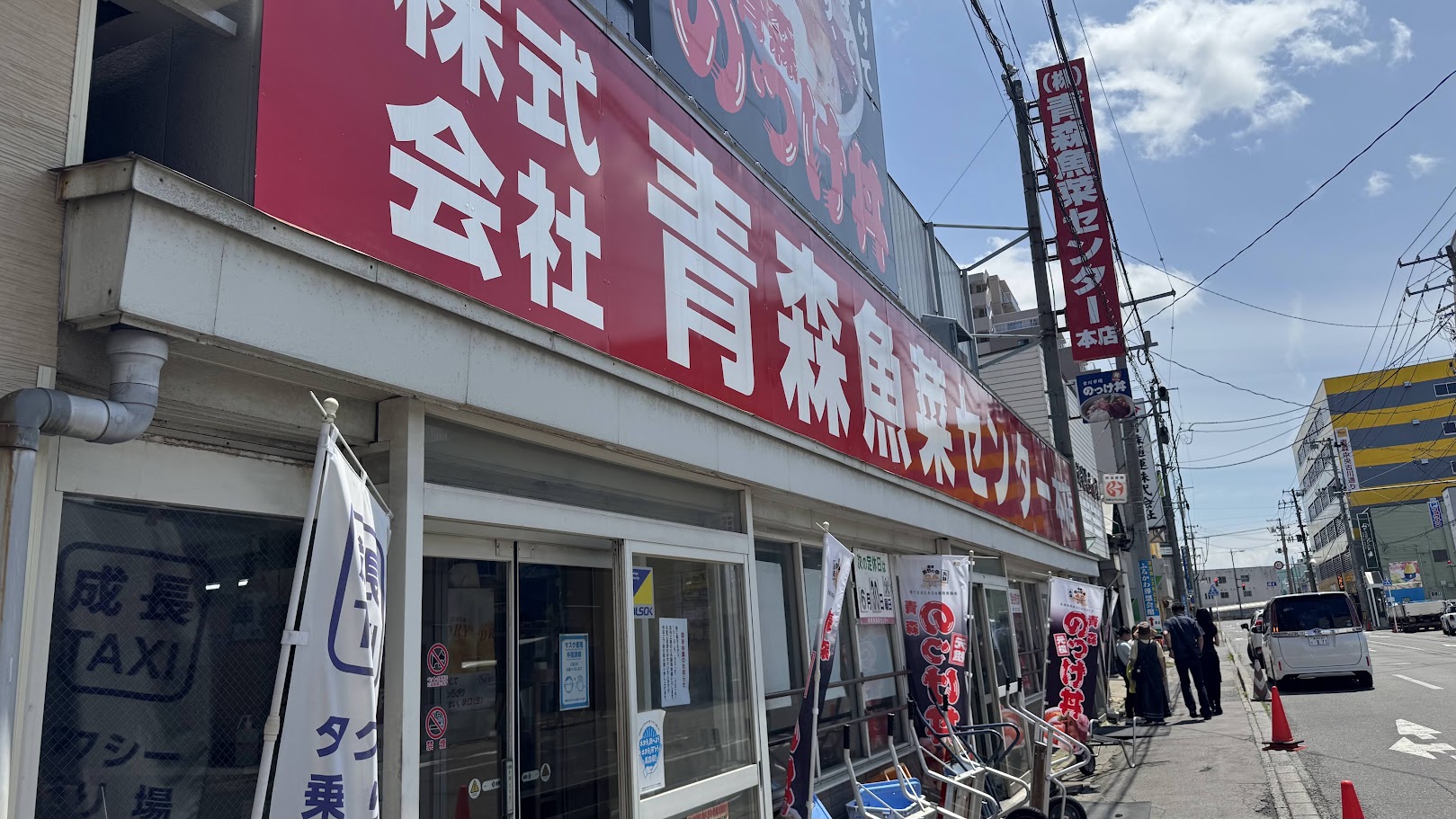 青森魚菜センターの外観。青空の下、赤い看板が目印