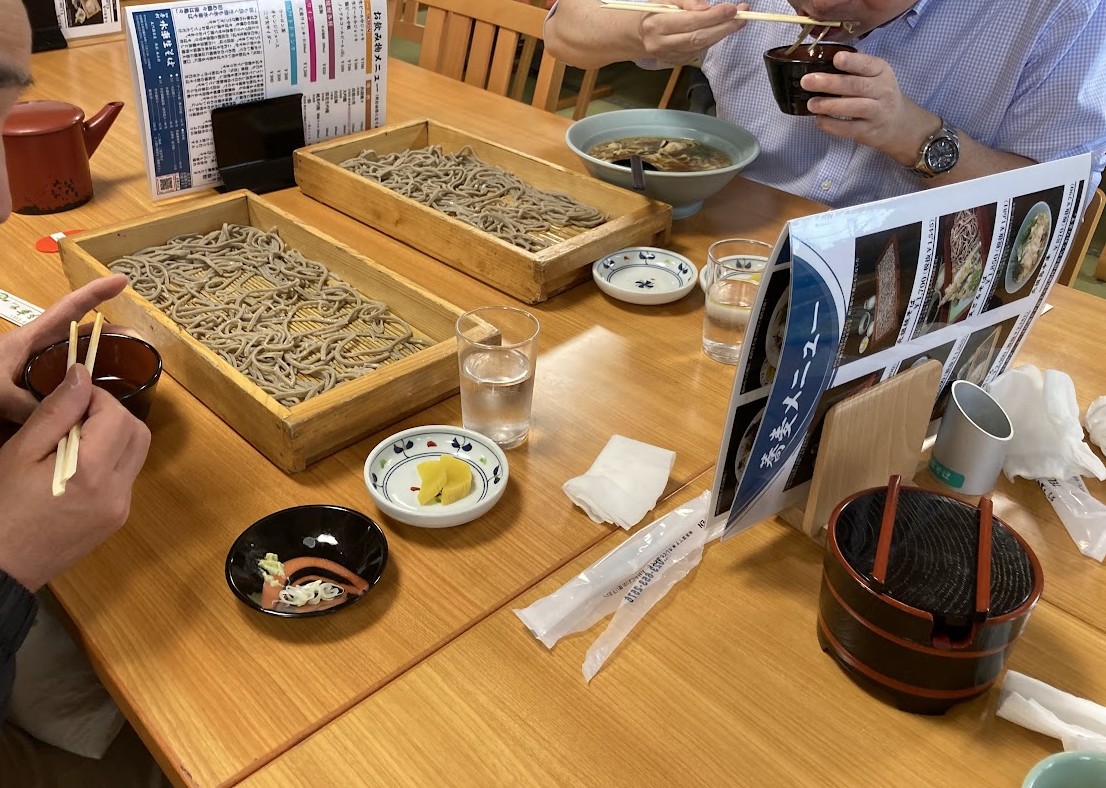 テーブルに並んだ板そばと鳥中華を、仲間と囲んでいる様子