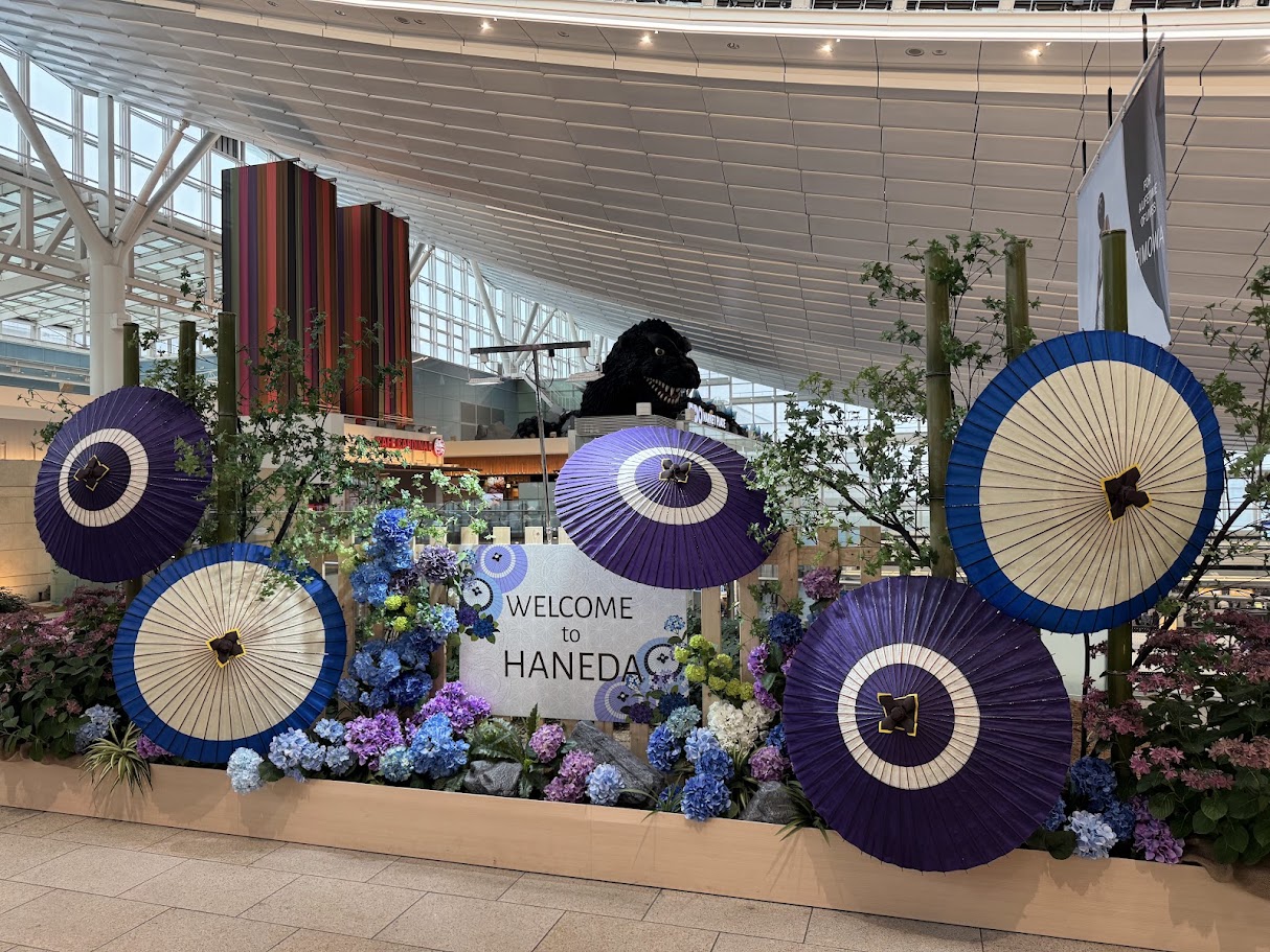 羽田空港の「WELCOME to HANEDA」の装飾。和傘と紫陽花が飾られ、奥にゴジラの頭も見える