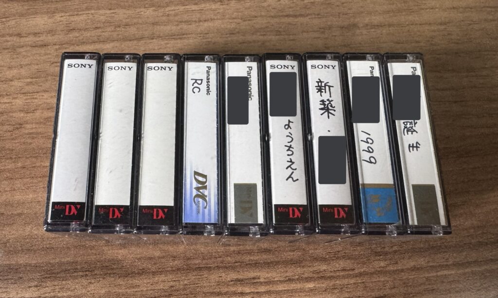 ケースに入ったMiniDVのカセットテープ9本を並べた写真。ラベルには誕生・1999・ようちえん・新築・RCと手書きされ、名前の部分は塗りつぶしてある