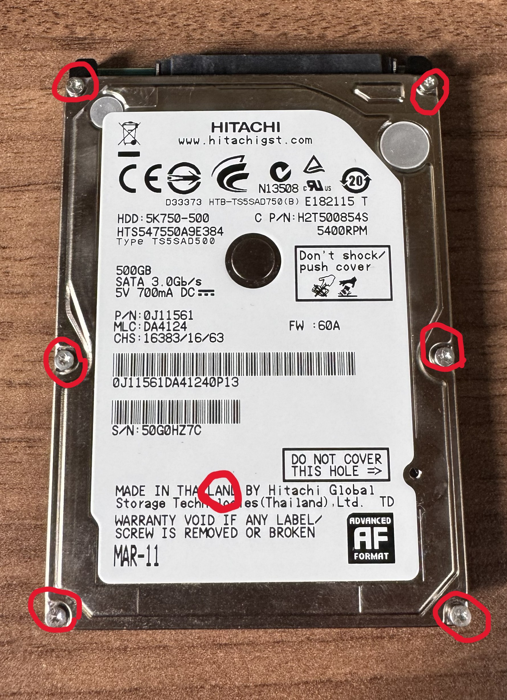 ノートパソコン用ハードディスクの表面。外周6本のネジと、ラベルの下に隠れていたネジの位置を赤い印で示している