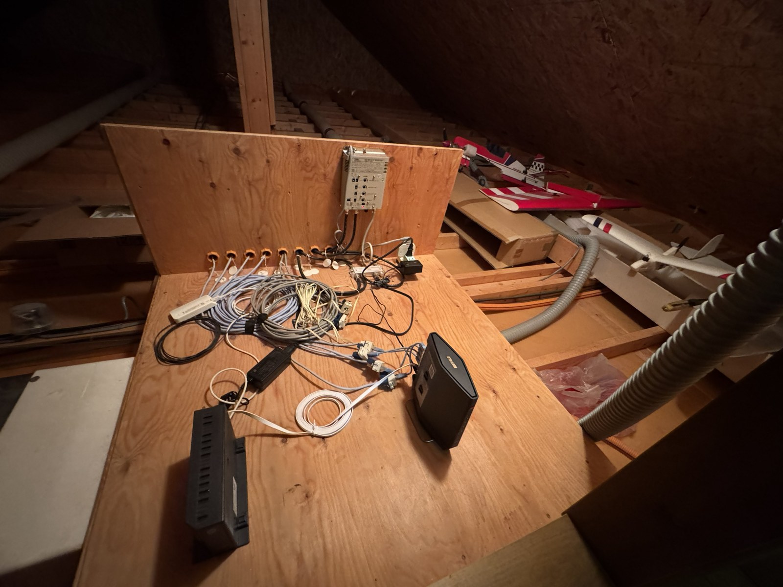 屋根裏の合板の上に置かれたルーターと機器、壁に並んだ8か所の配線用の穴と行き先を書いた札