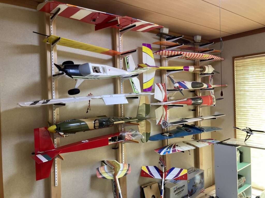 和室の壁一面に、2×4材の柱4本と棚受で十数機のラジコン飛行機を積んだ様子