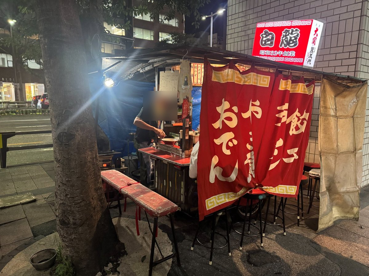天神の屋台「白龍」。看板に昭和32年創業、のれんに手造り餃子・おでん(店主の顔はぼかしている)